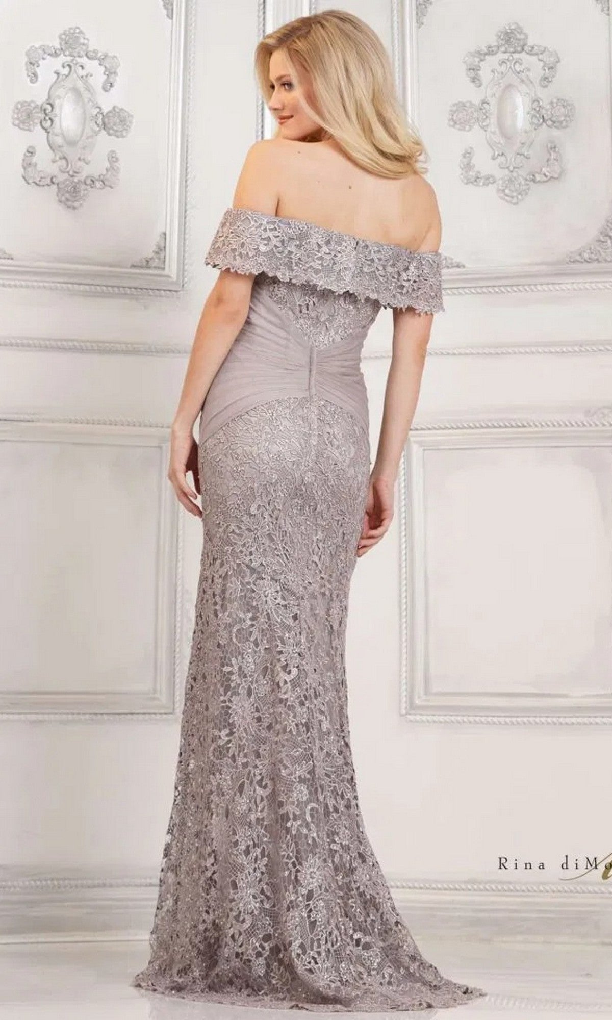 A woman in a Rina Di Montella RD3129 long formal dress stands facing away in an elegant, ornately decorated room.